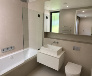 Modern bathroom refurbishment in London with floating vanity unit, bathtub with glass shower screen and contemporary tiled finish