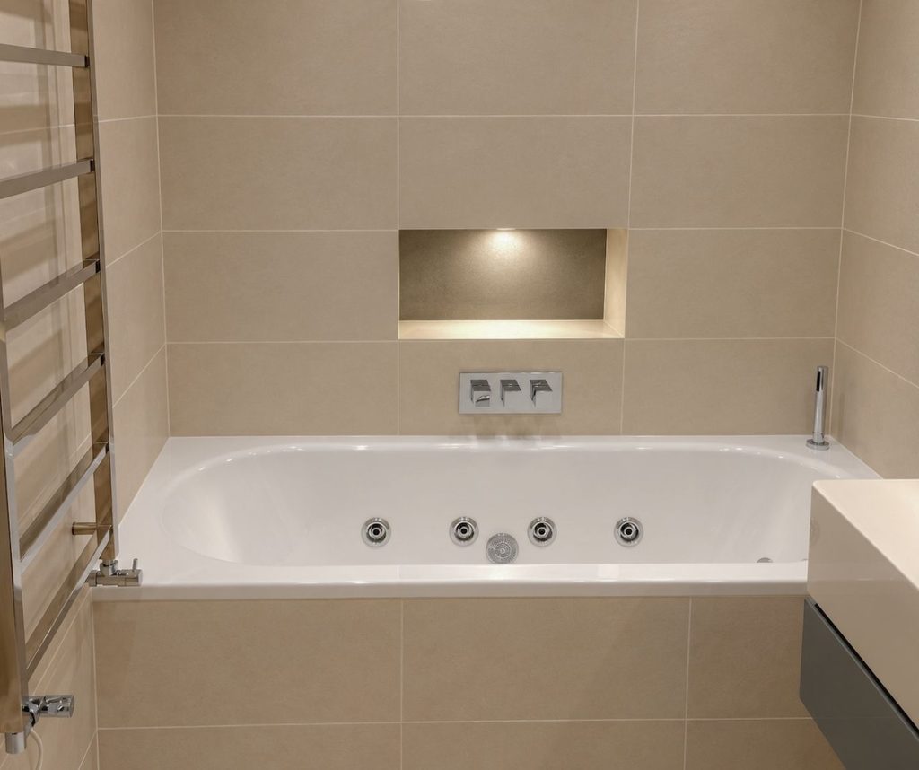Modern bathroom with whirlpool bath, tiled walls and recessed shelf lighting