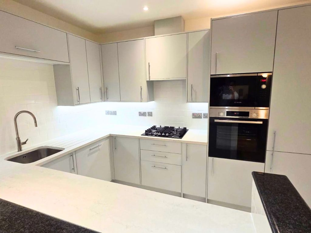 Kitchen after renovation with modern grey units, white worktops and integrated appliances